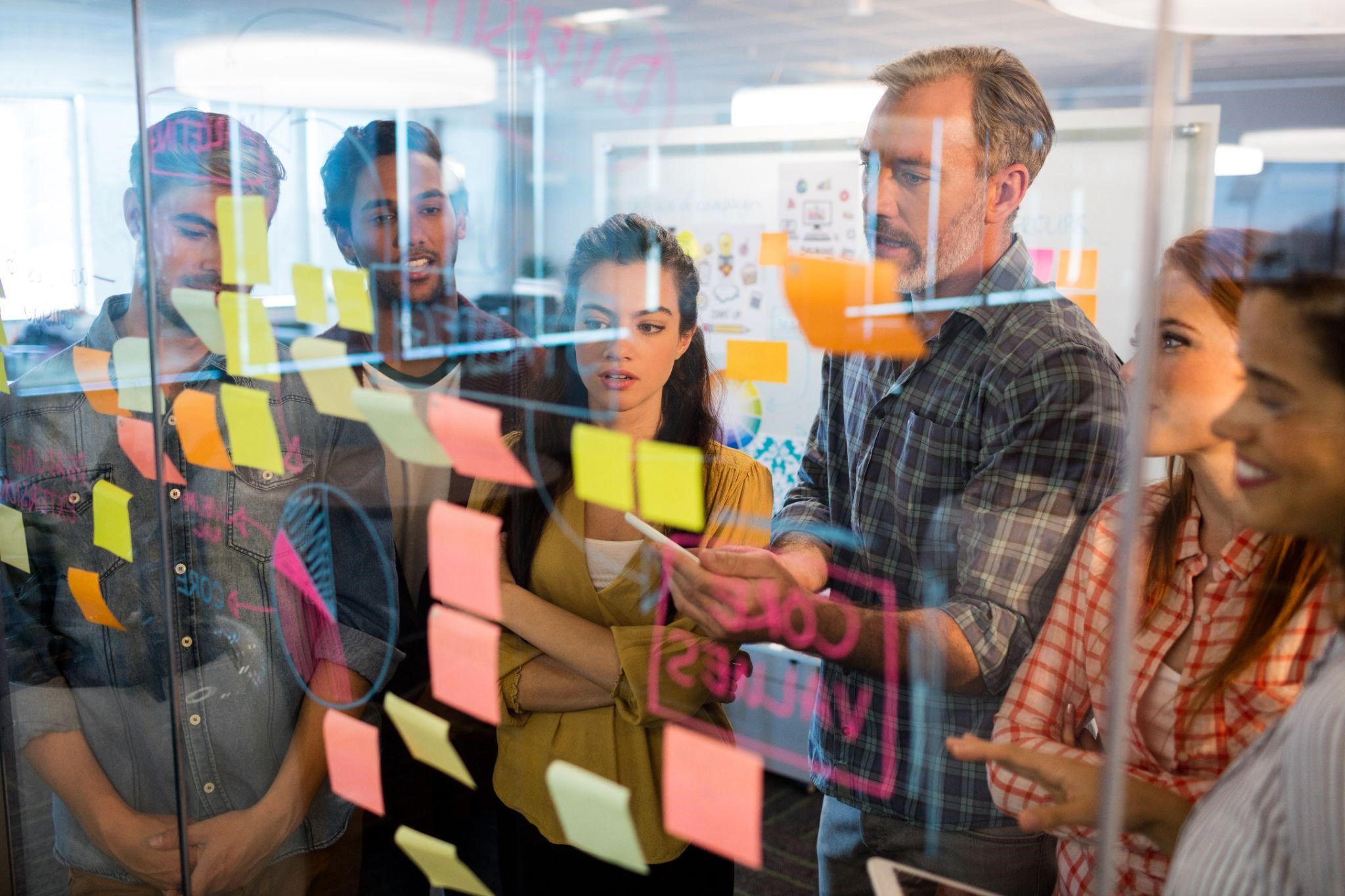 Team brainstorming session with sticky notes on a glass board during a product planning discussion