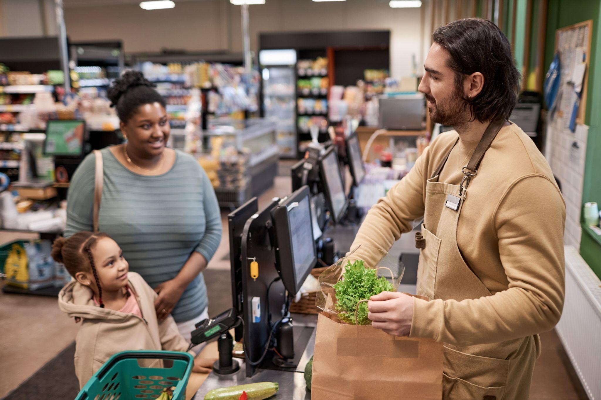 Grocery store cashier bagging items for a mother and child at the checkout counter