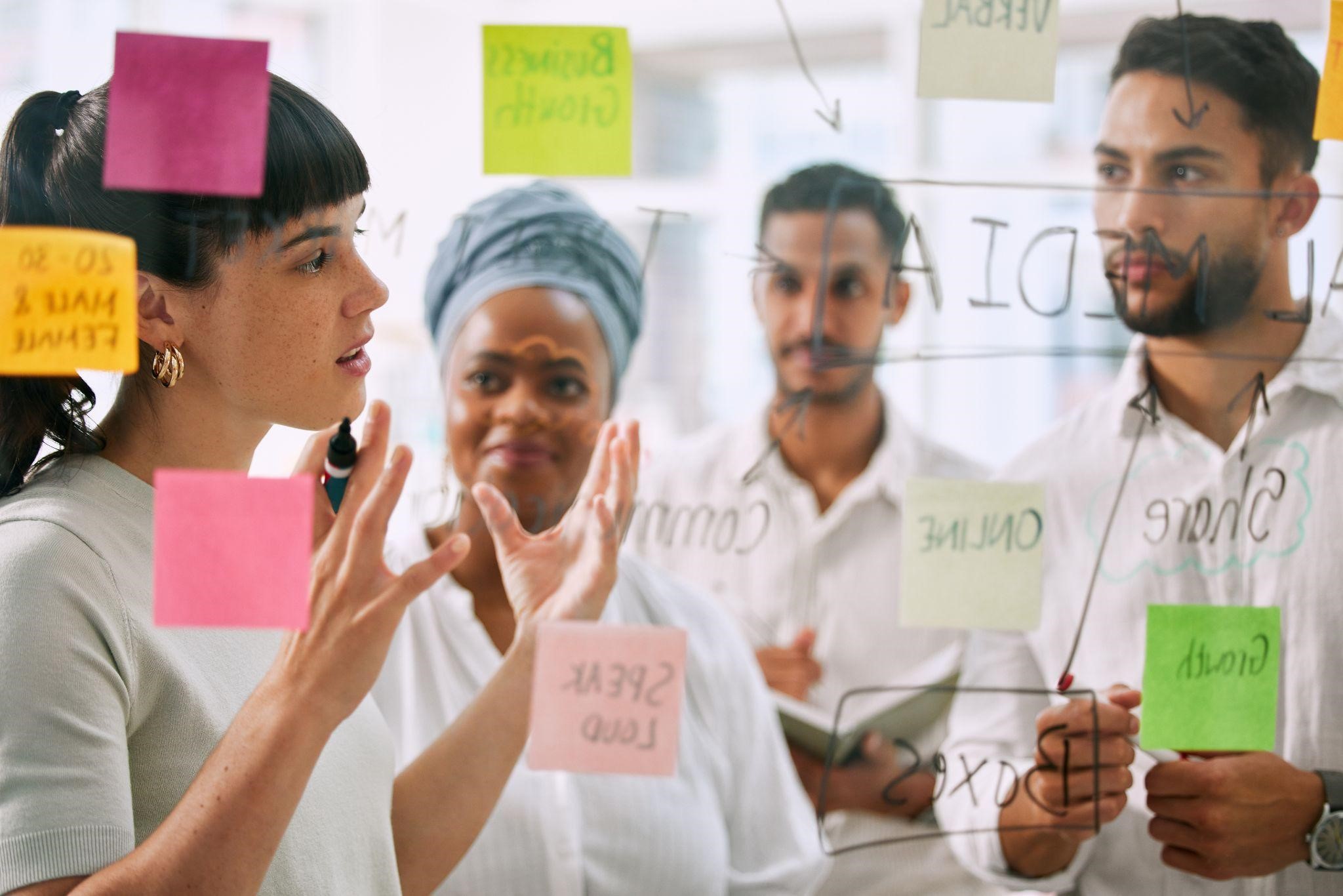Team discussing strategy ideas with sticky notes and handwritten diagrams on a glass board