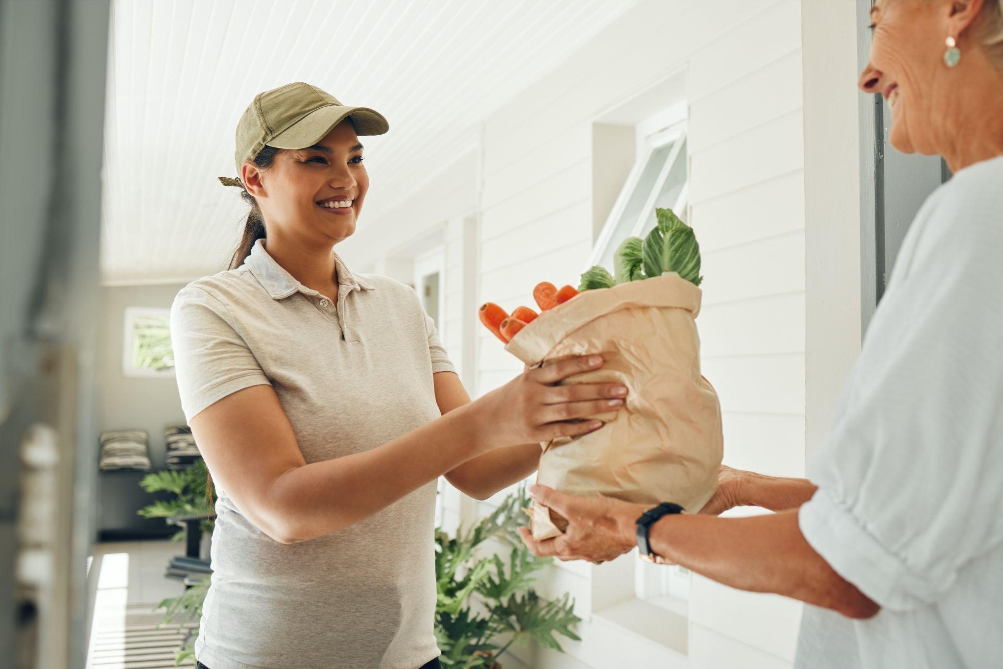 Delivery woman handing a bag of fresh groceries to a customer at her front door