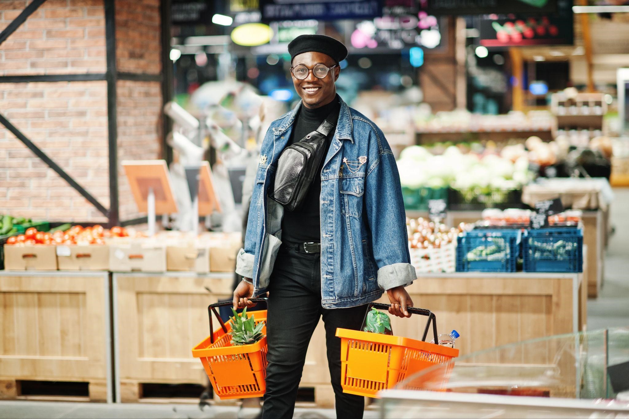 Smiling man holding two orange shopping baskets filled with groceries in a supermarket