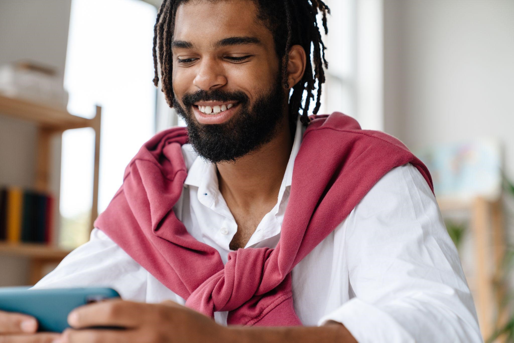 Smiling man looking down at his smartphone while sitting indoors