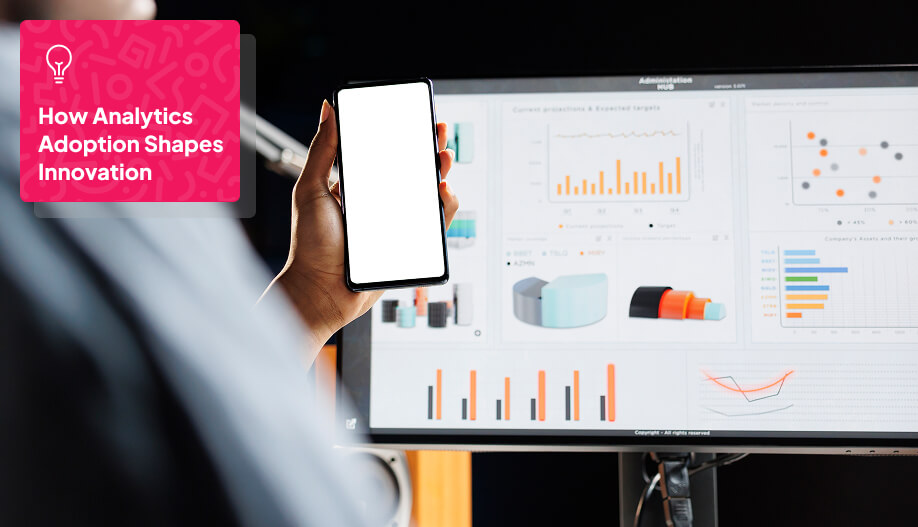 an employee looking at a computer screen showing different graphs while holding a cellphone